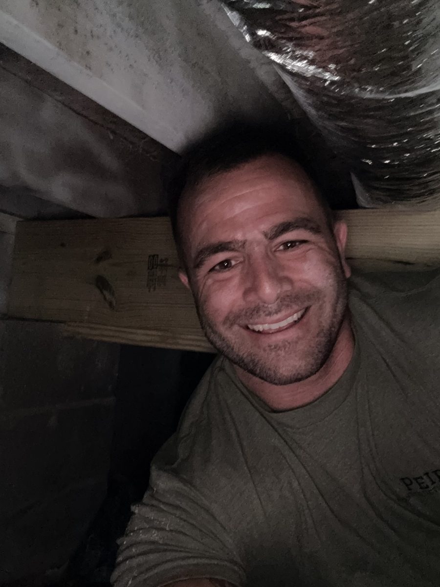 Kyle Peirson smiling from inside a crawlspace next to HVAC ductwork during an inspection