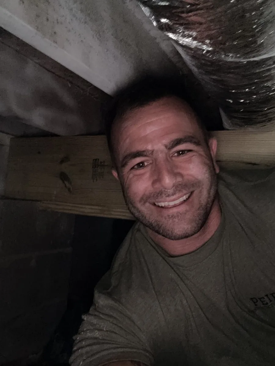 Kyle Peirson smiling from inside a crawlspace next to HVAC ductwork during an inspection