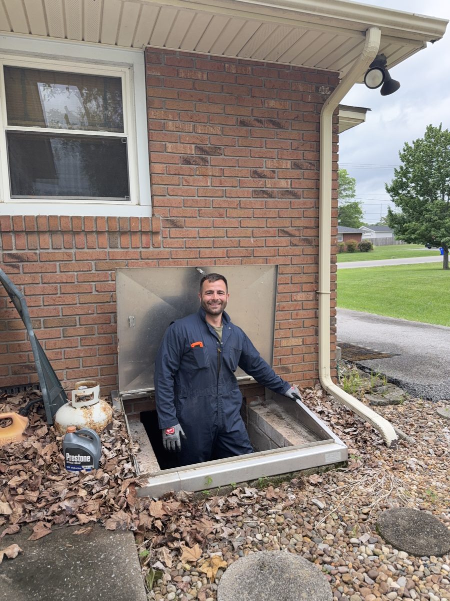 Kyle Peirson emerging from a basement access hatch during a home inspection