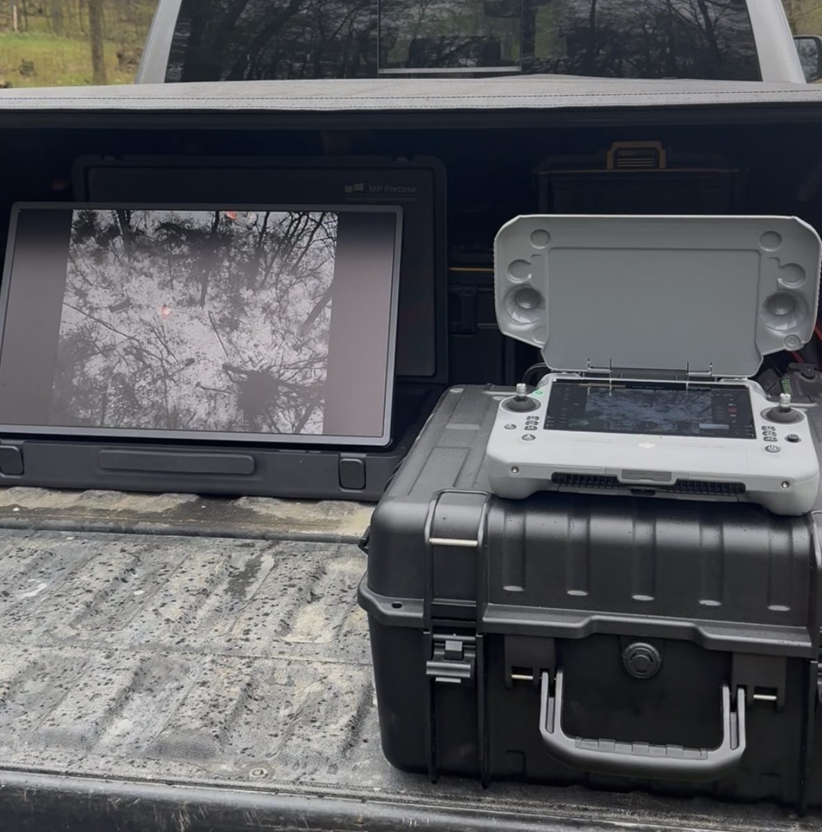 Thermal drone recovery field setup with controller and monitor showing thermal view of woods from a truck bed
