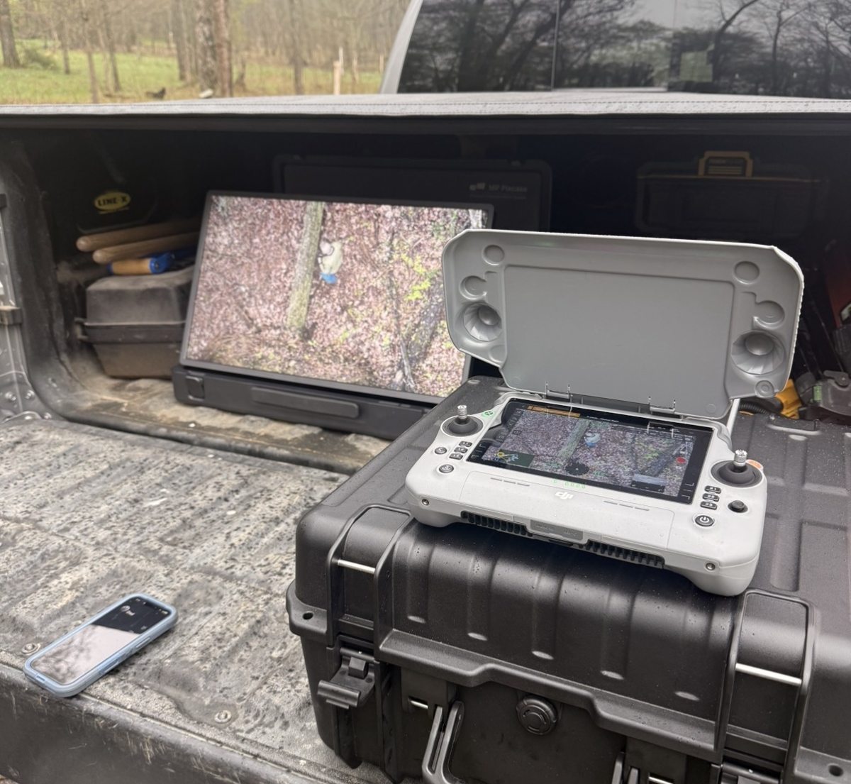 DJI drone controller displaying live zoom camera view of the woods during a recovery flight